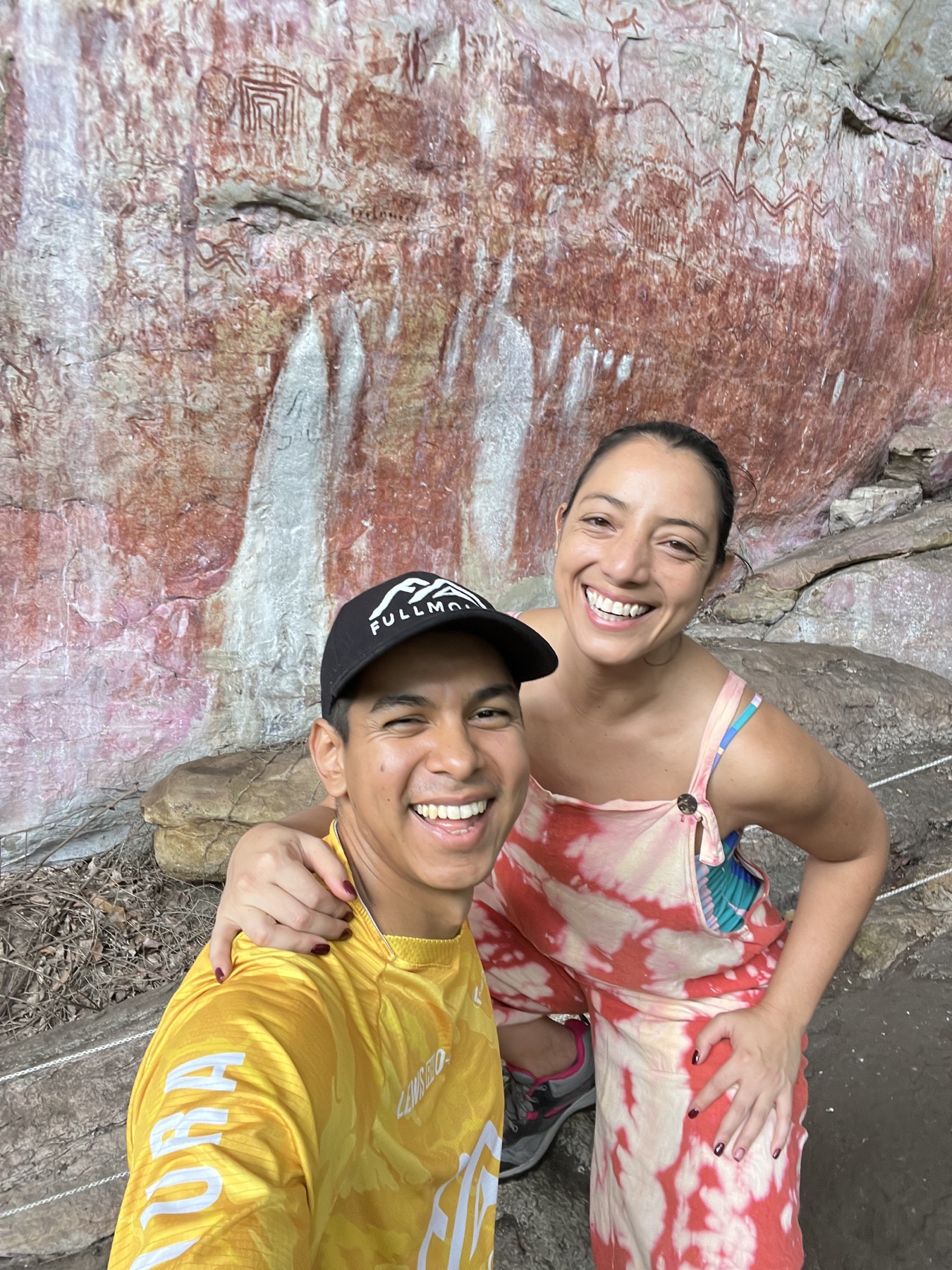 Laura y Lewis sonriendo frente a una pared de roca con pinturas