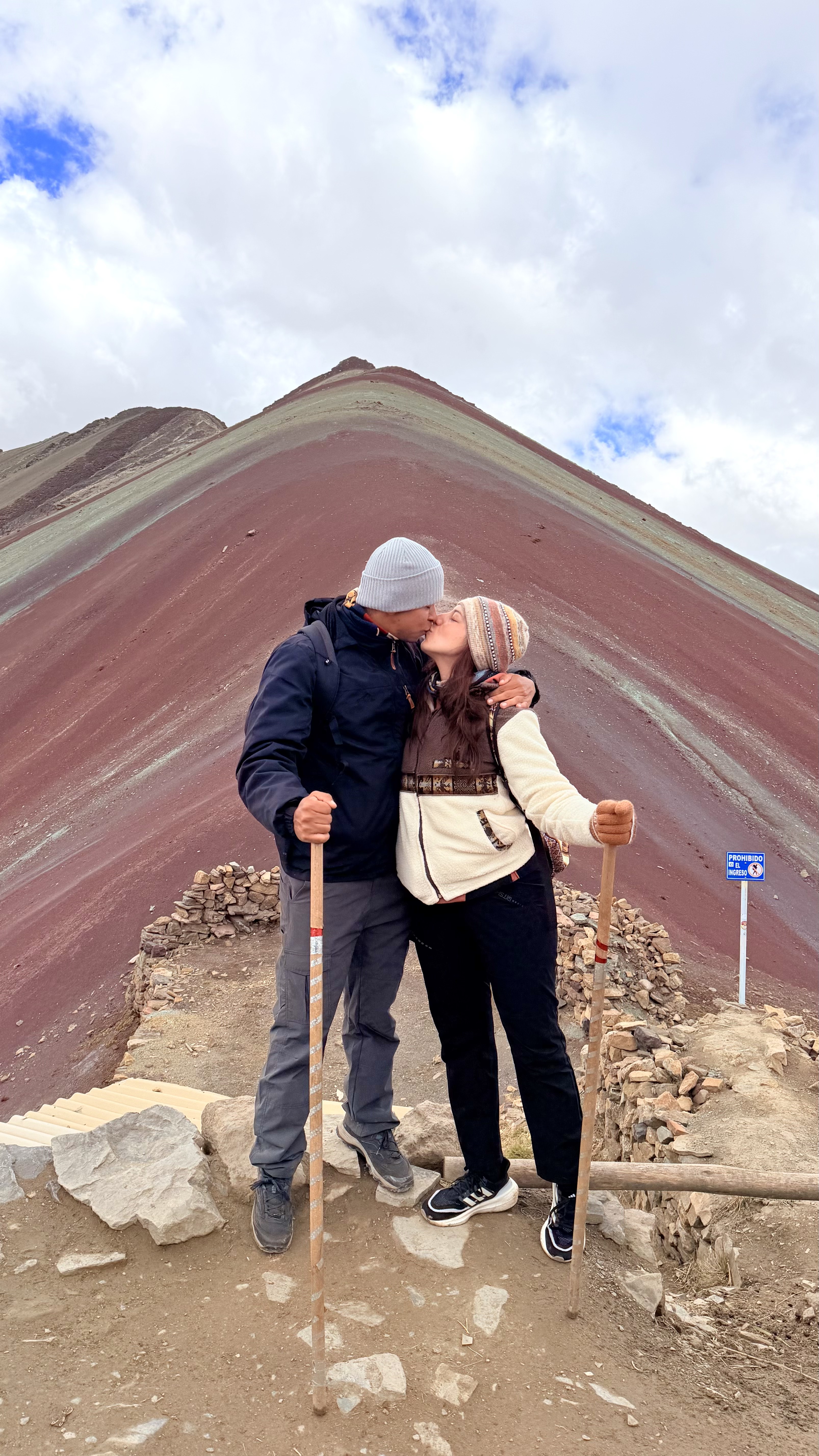 Laura y Lewis besándose frente a una montaña de colores